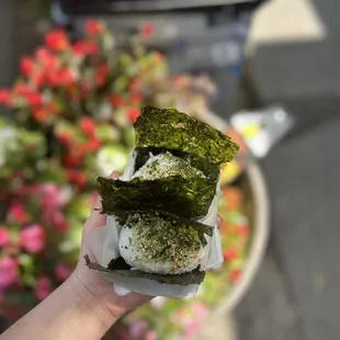 a hand holding a sandwich with seaweed