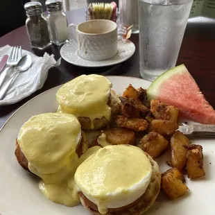 Traditional Eggs Benedict with home fries and a slice of watermelon.