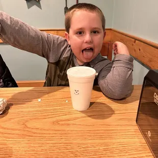 a young boy sitting at a table with a cup of coffee