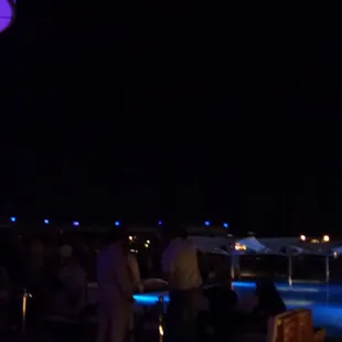 a crowd of people standing around a pool at night