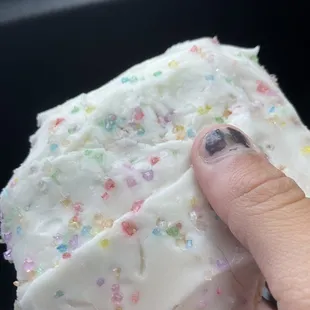 a hand holding a frosted donut with sprinkles