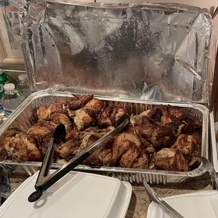 a pan of chicken in foil with tongs