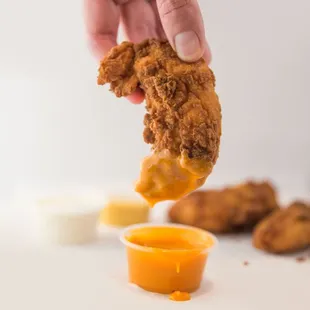 a hand dipping a fried chicken nugg