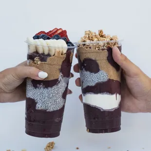 two hands holding two cups of ice cream and fruit