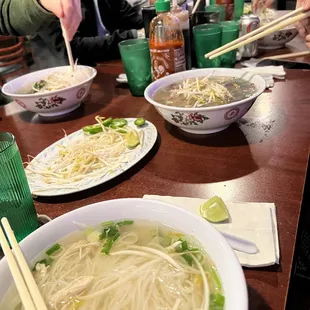 a group of people sitting at a table with bowls of soup and chopsticks