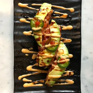 an avocado covered in sauce on a black plate