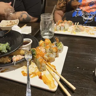 two people sitting at a table with plates of sushi and chopsticks