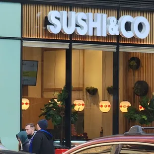 people walking in front of a sushi and co store