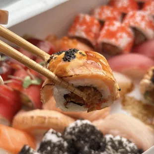 a person holding chopsticks over a box of sushi