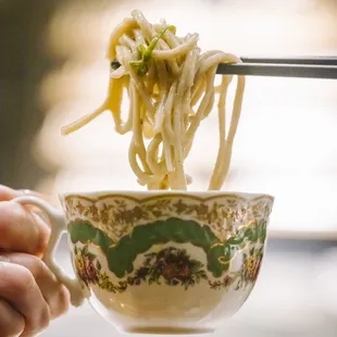 a bowl of noodles being lifted by a pair of chopsticks