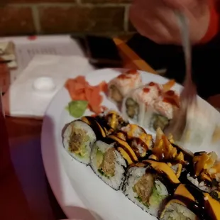 a plate of sushi with a hand holding a knife