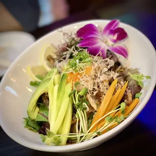 a bowl of salad with a purple orchid