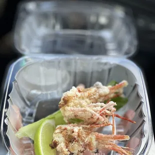 a plastic container with shrimp and a lime wedge