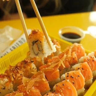 a person holding chopsticks over a tray of sushi