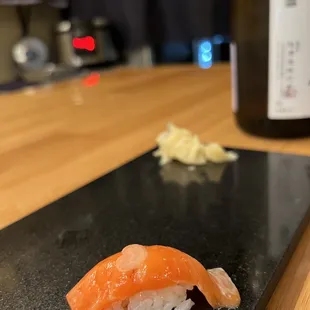 a sushi on a black plate with a bottle of wine in the background