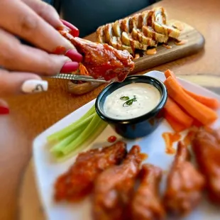a plate of chicken wings, carrots, celery and dip