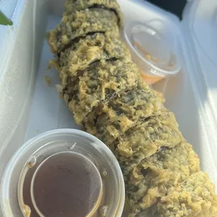 a close up of a sushi roll with sauce in a styrofoam container