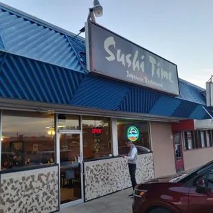a man holding an umbrella in front of a sushi time restaurant