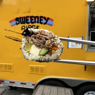 a person holding a sushi roll in front of a food truck