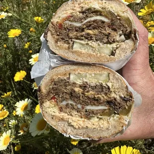 a hand holding a sandwich in a field of flowers