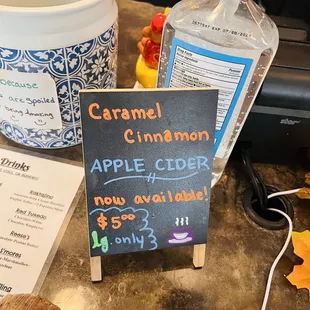a chalkboard with a sign that says caramel cinnamon apple cider now available