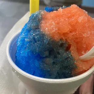 a person holding a plastic cup filled with blue and orange ice cream