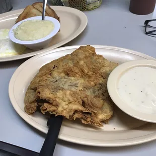 Chicken fried steak and eggs with toast, gravy, and grits.