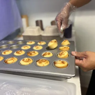 a person putting icing on top of a muffin tin