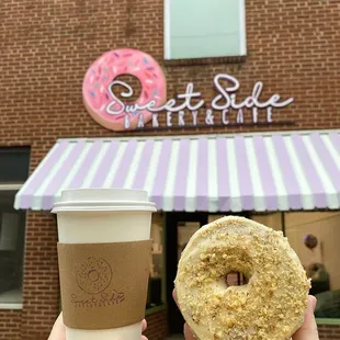 a hand holding a donut and a cup of coffee