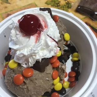 Oreo brownie sundae with chocolate gelato topped with Reese pieces, snickers whip cream and a cherry.