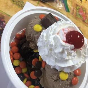 Oreo brownie sundae with chocolate gelato topped with Reese pieces, snickers whip cream and a cherry.