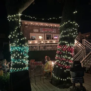 people sitting at a table in front of a house decorated with christmas lights