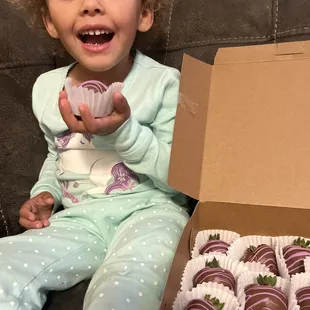 a little girl holding a box of chocolate covered strawberries