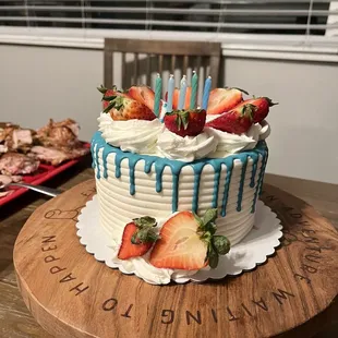 a birthday cake with strawberries and blue drips