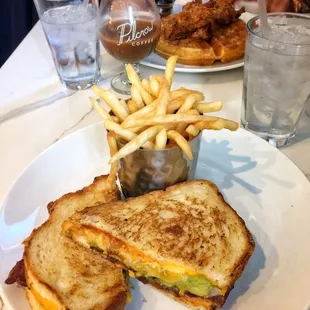 Grilled cheese wth bacon and avocado, and the background is sweet cream cold brew + cornbread waffles with Memphis style fried chicken.