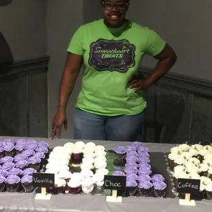 a woman standing in front of a table with cupcakes