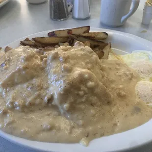 Biscuits and gravy with two eggs over easy and country potatoes.