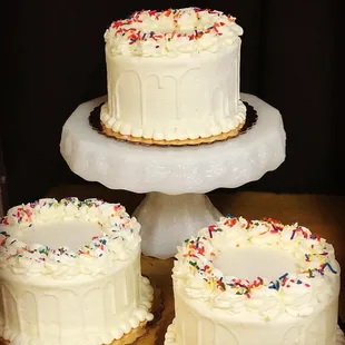 three white frosted cakes with sprinkles