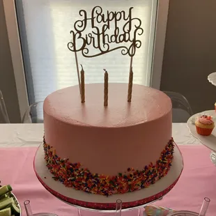 a pink birthday cake and cupcakes