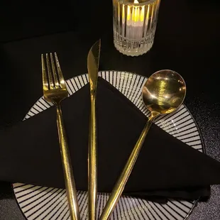 a place setting with gold cutlers and a candle