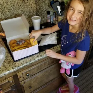 a little girl standing in front of a box of donuts