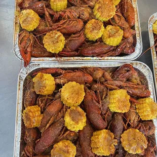 three trays of cooked crawfish and corn