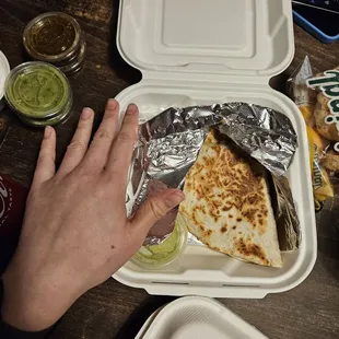 a person grabbing a burrito out of a styrofoam container