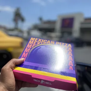 a hand holding a box of mexican pizza