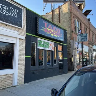 a black car parked in front of a pizza shop