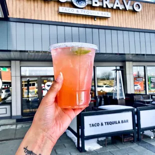 a hand holding a drink outside a taco bravo restaurant
