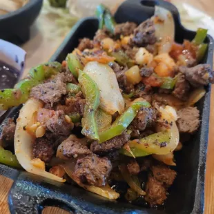 meat and vegetables in a black dish