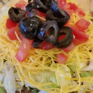 a taco with black olives, tomatoes, lettuce, and cheese