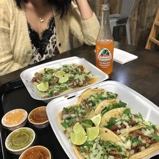 a woman sitting at a table with two plates of tacos