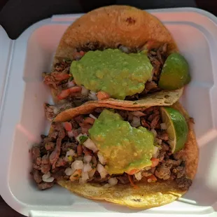 Two tacos: carnitas (top) and carne asada (bottom), both served with a dollop of guacamole and light pico de gallo.